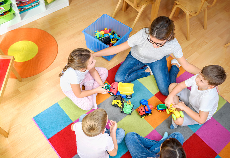 A teacher sitting on a floor in a circle with three students.