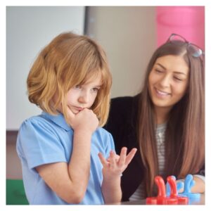 Young girl counts on fingers while teacher smiles behind her