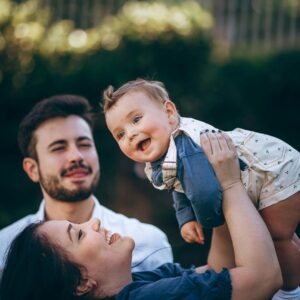 A young couple smiling at their child outside.