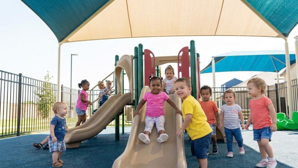 A diverse group of toddlers playing happily on a modern, shaded playground structure.