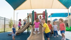 A diverse group of toddlers playing happily on a modern, shaded playground structure.